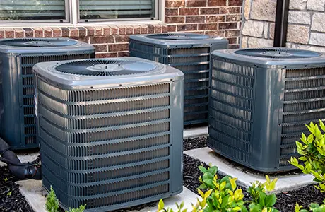 Four air conditioning units in front of brick facade.