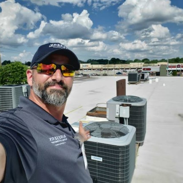 Aire Serv Employee on roof in front of AC condensers.