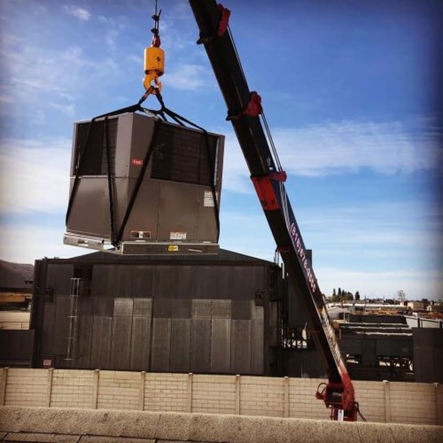 Crane holding new rooftop unit.