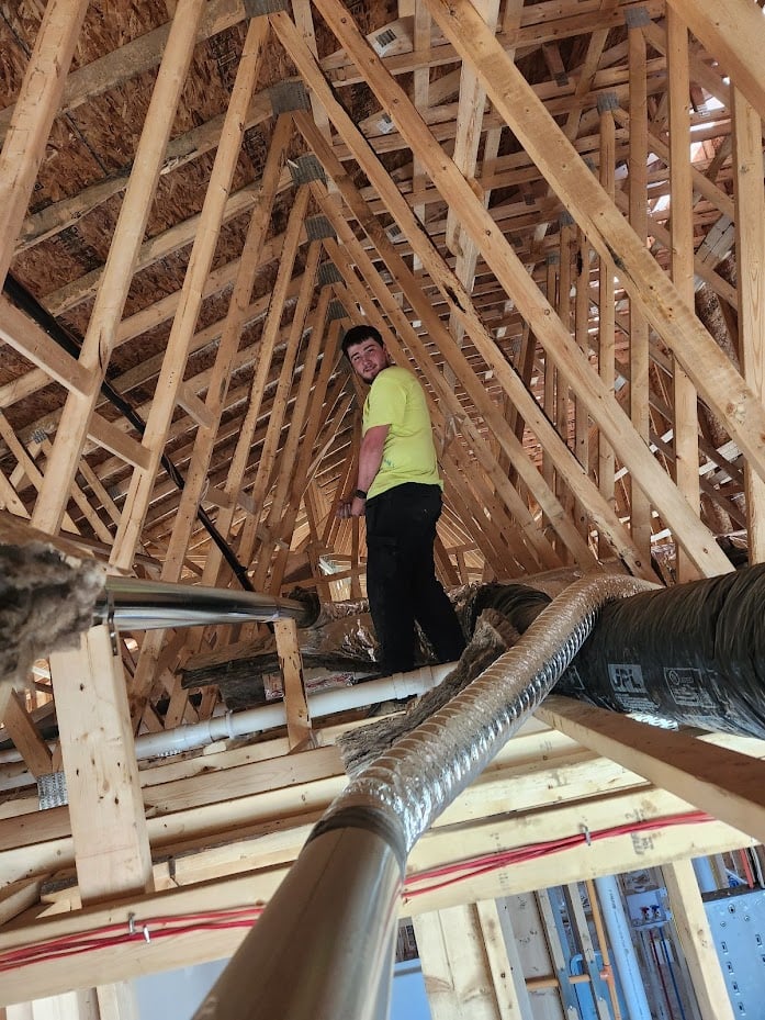 Technician in an attic check the air ducts on a new construction site.