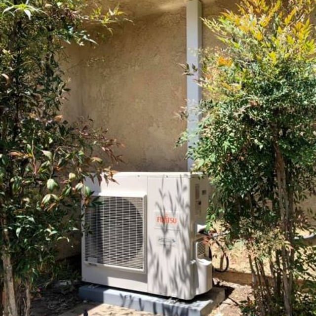 New heat pump system installed outside of home between bushes.