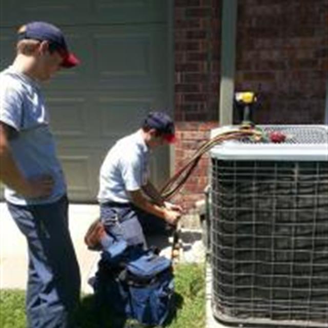 Service tech Jordan repairs an Aire Serv customers A/C unit, while apprentice Colton hands him tools