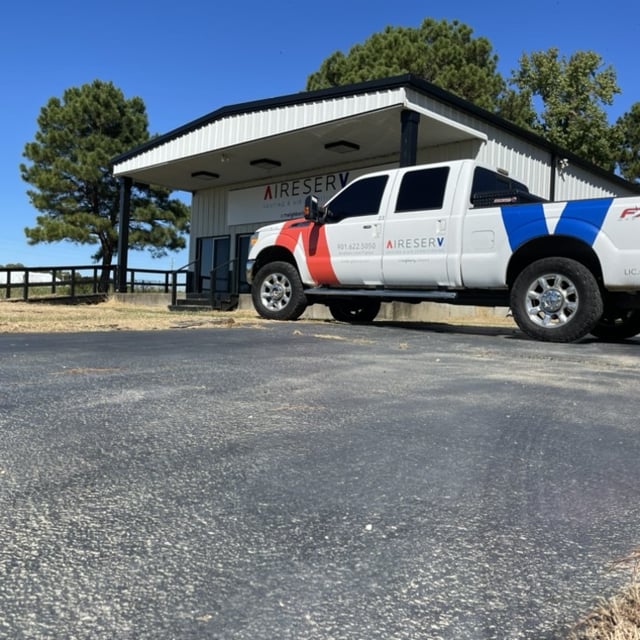 white truck with aire serv logo parked in front of building with aire serv sign