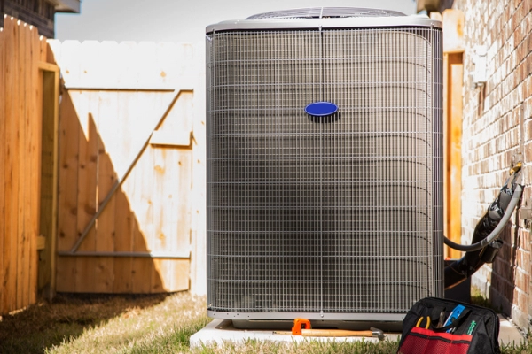 Air conditioner unit outdoors inside yard of a brick home. Repairman's tools, toolbox beside the unit | Aire Serv of Wilmington