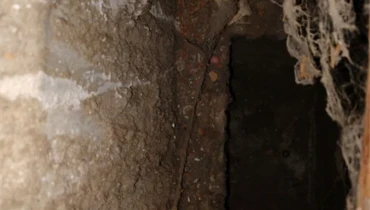 Brown dust and debris hanging from the interior sides and top of a dirty HVAC system.