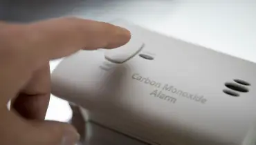 A close-up view of a hand pressing a button on a white carbon monoxide alarm. | Aire Serv of North Central Arizona