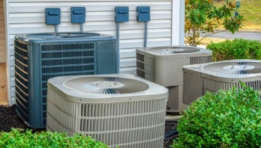 The outdoor condenser coils of four air conditioners are shown next to an apartment complex. | Aire Serv of Citrus County