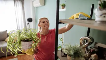 A woman uses a microfiber cloth to wipe dust off a shelf in her home. | Aire Serv of North Central Arizona