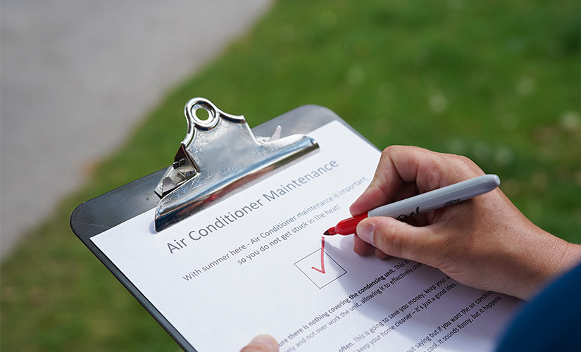 Person checking off box on paper that reads: Air Conditioner Maintenance