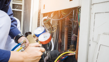 Close-up of technician holding manifold gauge beside HVAC system.