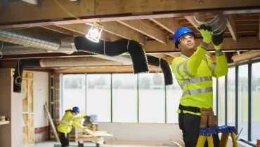 An HVAC technicians installs ductwork wearing safety gear.