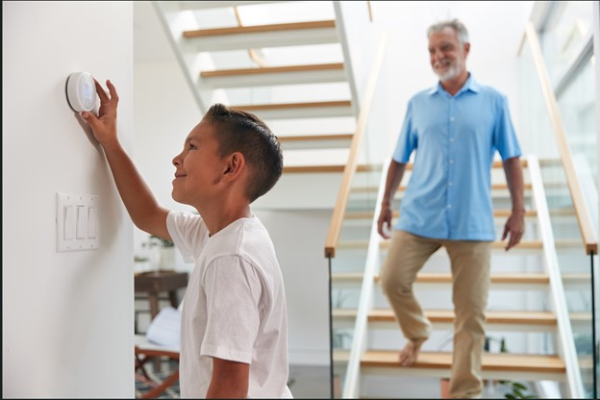 Little boy playing with thermostat as grandpa watches while coming down the stairs.