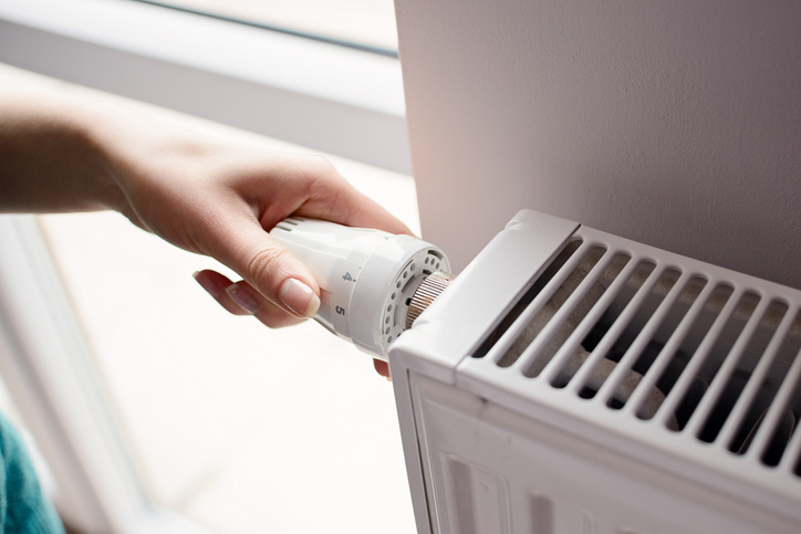 A close-up of a person’s hand adjusting the thermostat valve knob on the side of a radiator. | Aire Serve of North Central Arizona