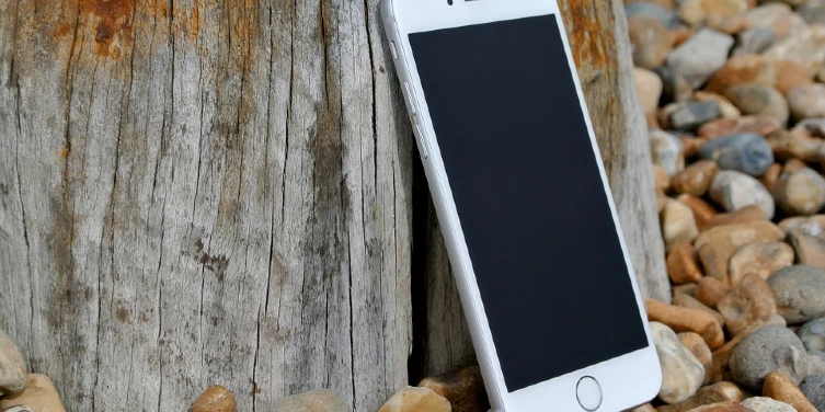 iPhone leaning against stump on pebbles.