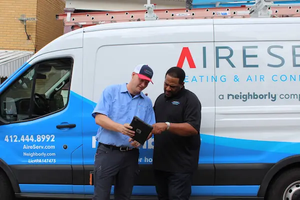 NFL great Jerome Bettis reviewing chart with Aire Serv service pro with Aire Serv van in background.