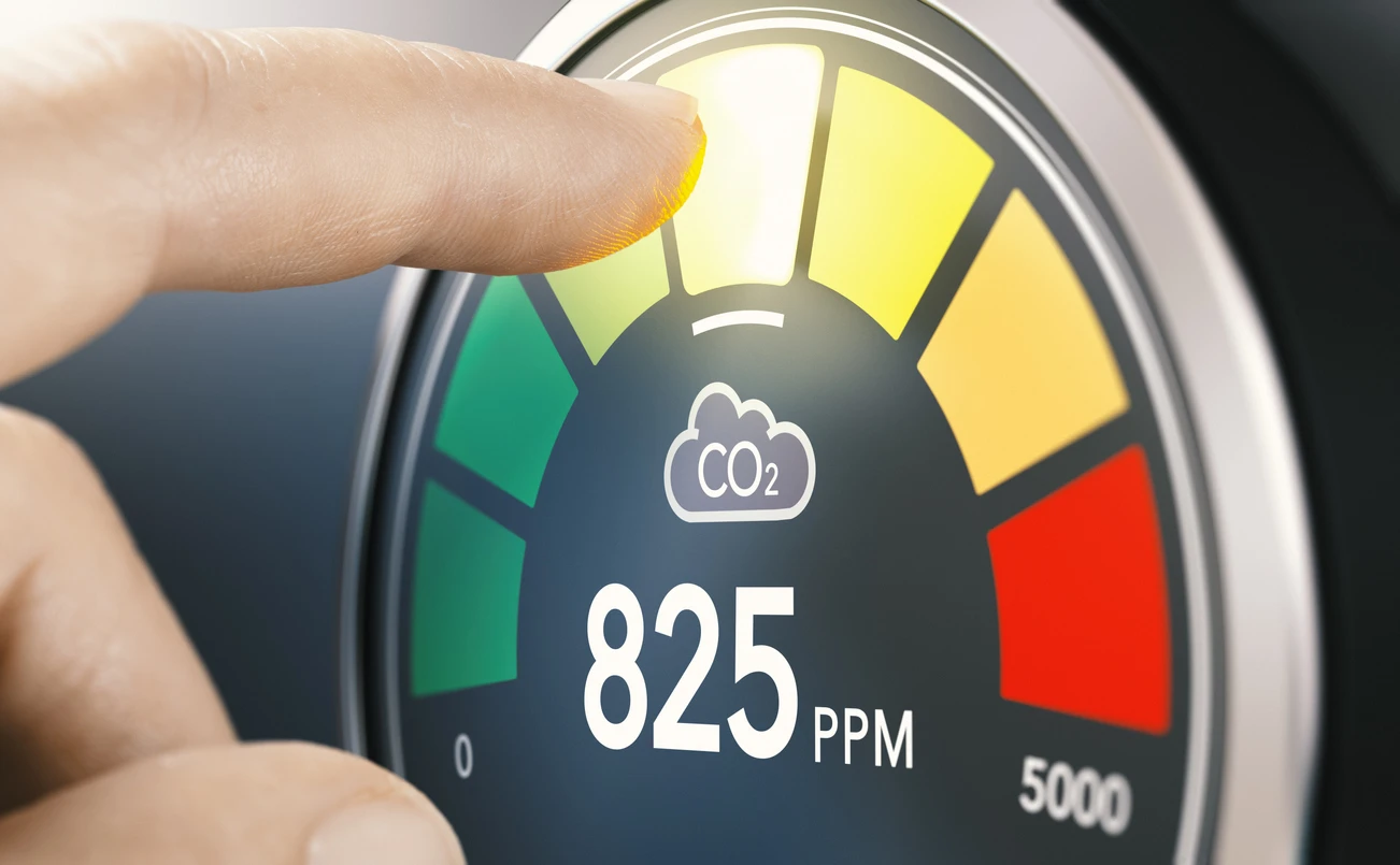 A finger presses the CO2 button on a digital IAQ meter.