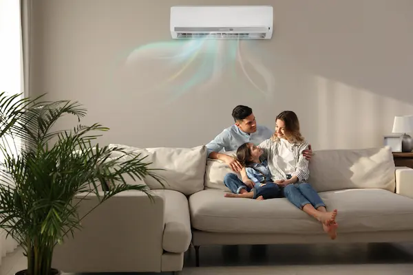 A family rests on the couch while their air conditioner blows cool air into the room.