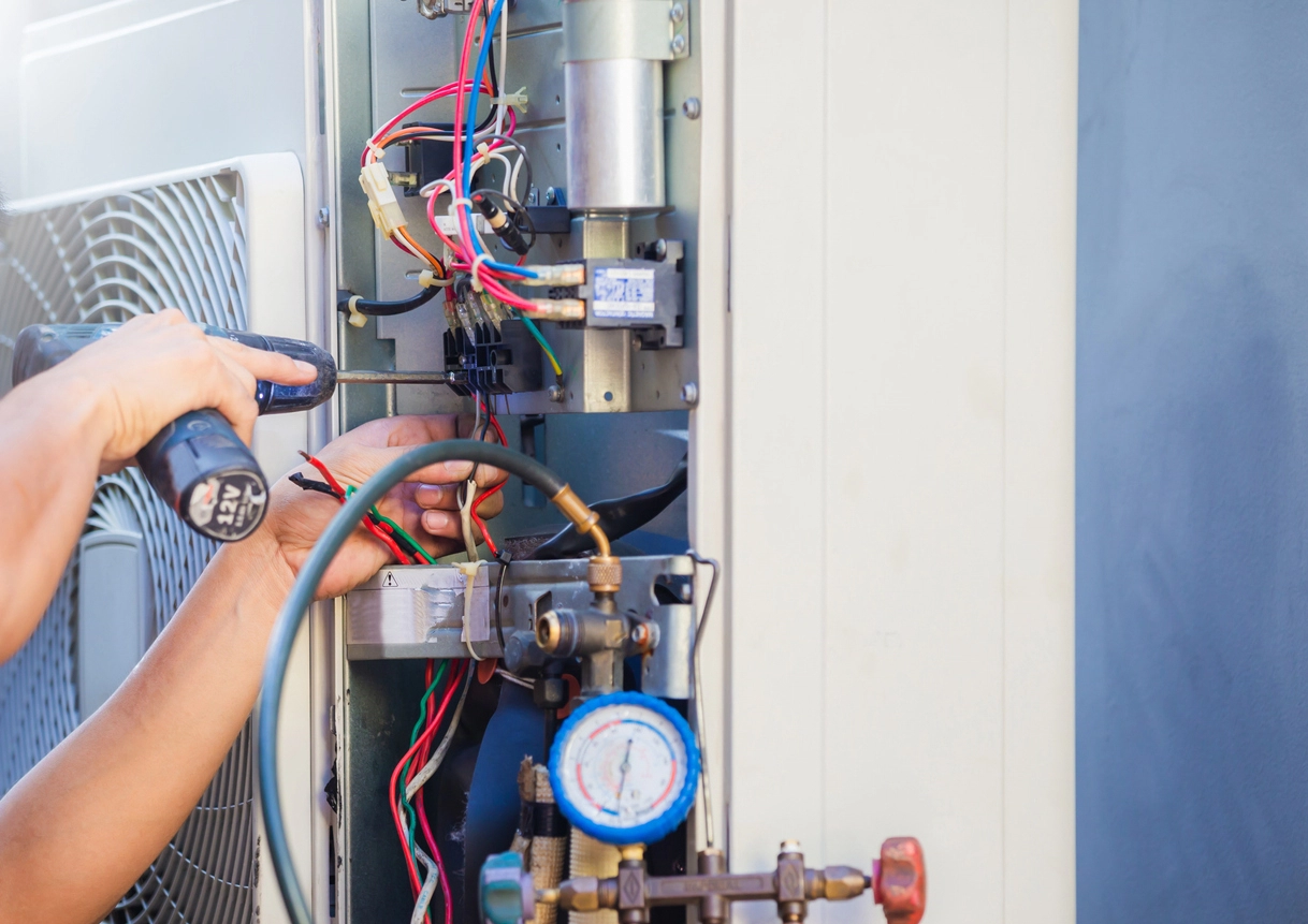 Close-up of handyman with hand drill repairing outdoor HVAC unit.