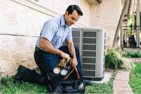 Aire Serv technician removing manifold gauge from tool bag beside large outdoor HVAC unit.