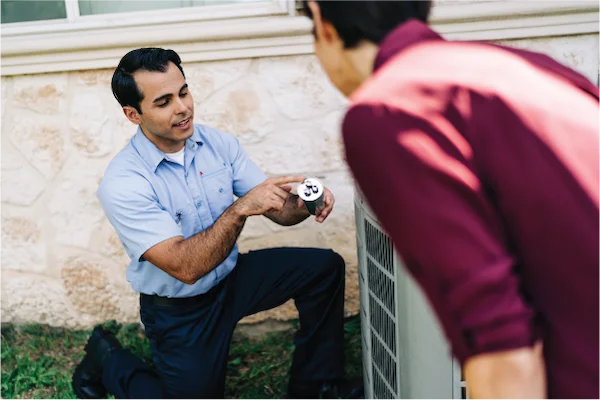 Aire Serv technician kneeling beside outdoor HVAC unit and customer in burgundy shirt.