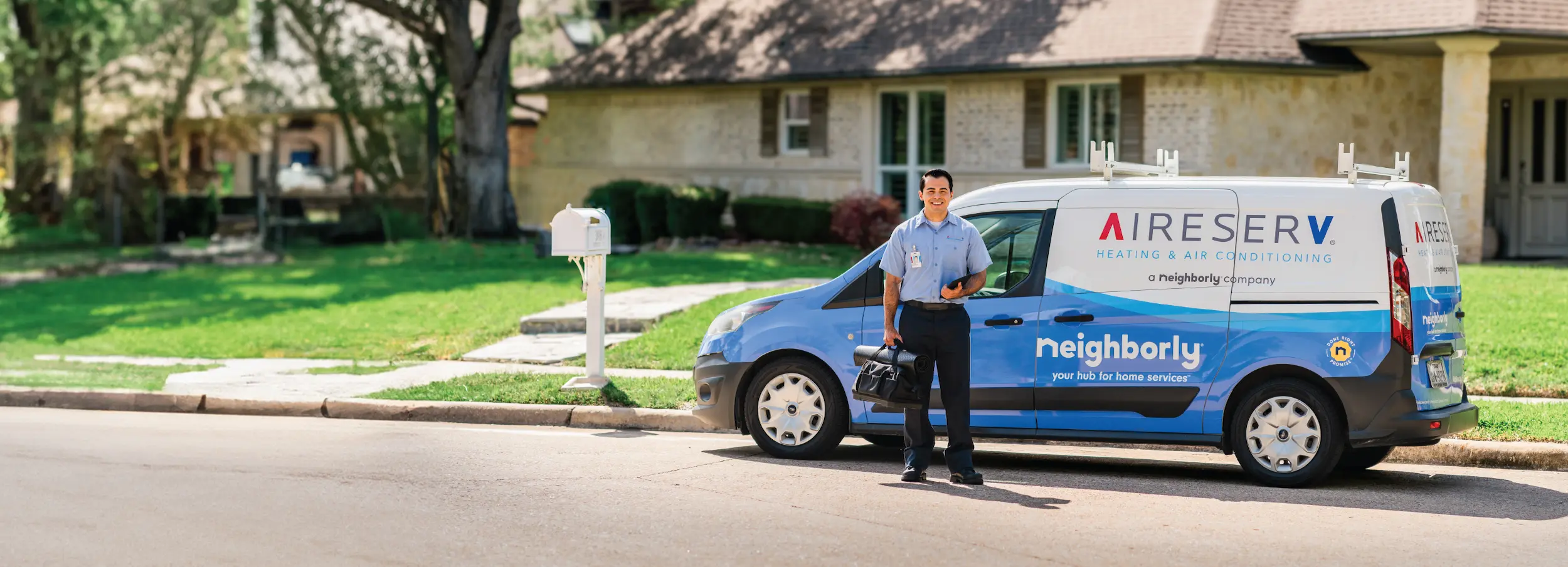 Smiling Aire Serv technician standing beside branded van arriving for residential service call.