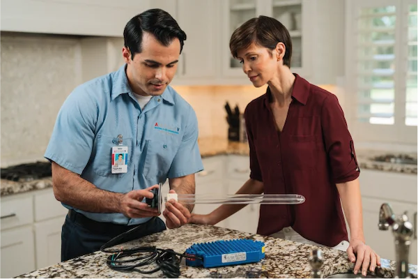 Aire Serv professional and female customer inspecting indoor air quality device on kitchen countertop.