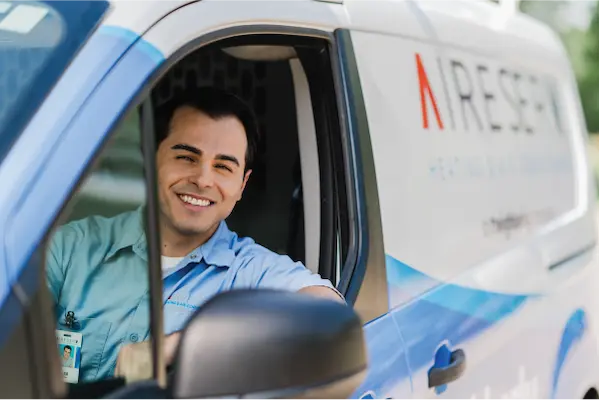 Smiling male Aire Serv technician leaning out of driver's seat window of branded van.