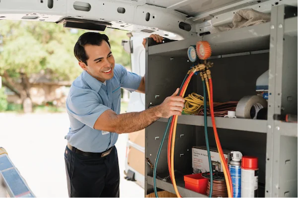 Male Aire Serv technician reaching for manifold gauge inside van.