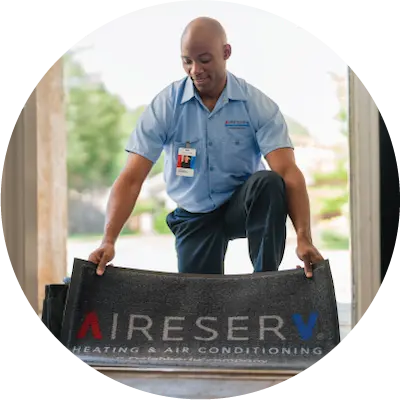 Male technician placing Aire Serv branded rubber mat on floor.