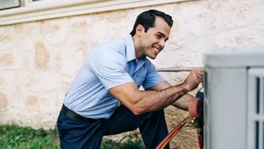 Smiling male HVAC technician inspecting large outdoor unit.