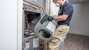 Male technician wearing disposable dust mask replacing HVAC blower motor.