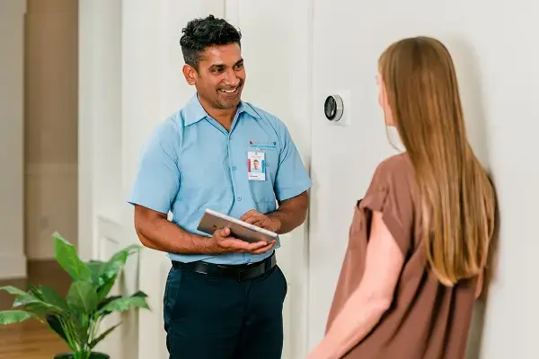 Aire Serv tech and female customer standing beside wall mounted thermostat.