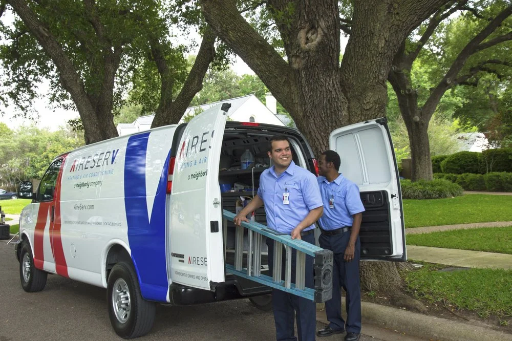 Two HVAC service professionals from Aire Serv unloading a ladder and other equipment from the back of a work van.