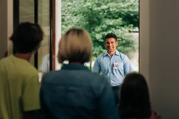 Smiling male Aire Serv technician greeting family framed by doorway.