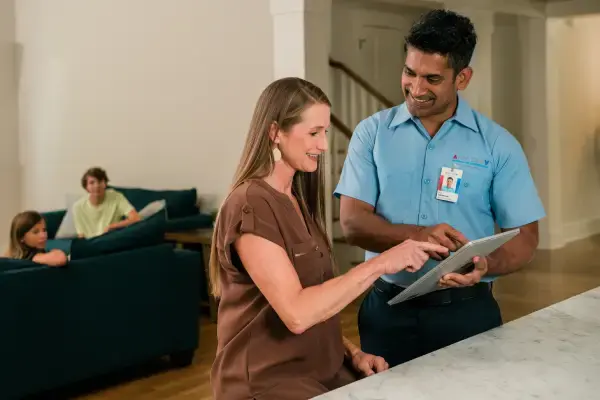 Male technician and female customer pointing at tablet device in living room with childen sitting in background.